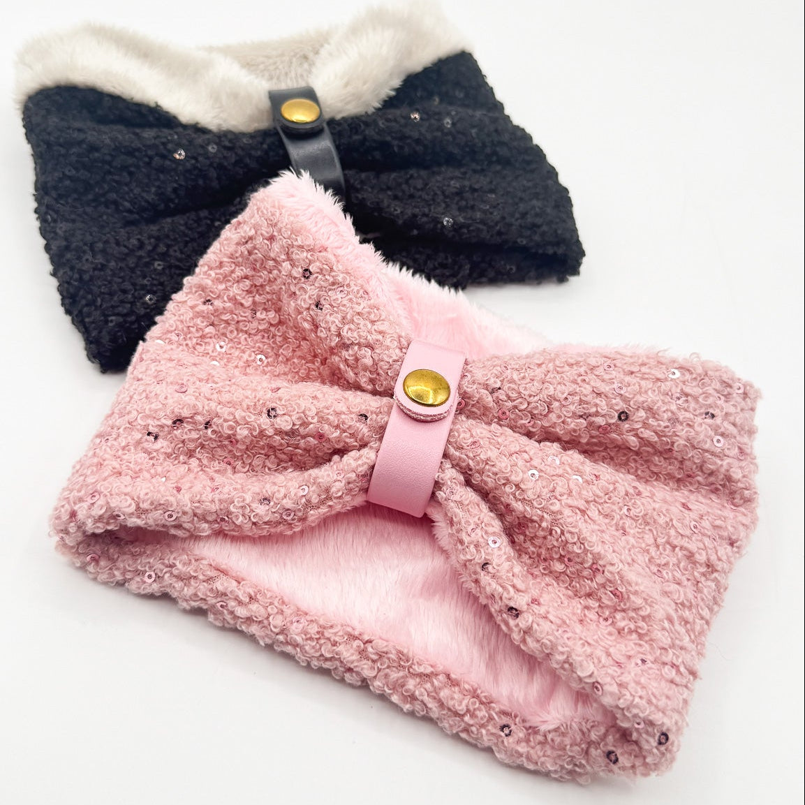 Due scaldacollo Cocoon per cani piccoli in bouclé con paillettes: uno rosa con interno in pelliccia rosa, uno nero con interno in pelliccia panna, con passante in ecopelle e bottone dorato